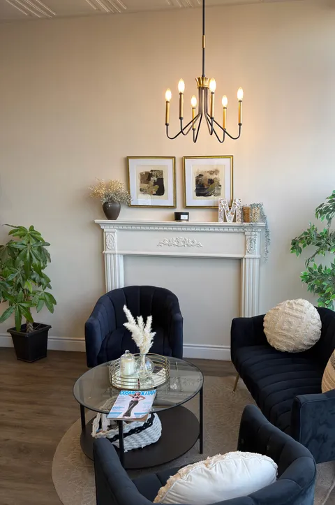 Waiting area with navy velvet armchairs, a brass chandelier and a white mantel